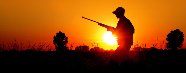 A silhouette of a male hunter carrying a shotgun. He could be hunting pheasant, chukar, partridge,...