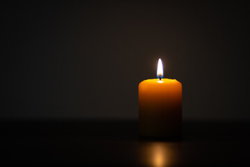 Yellow candle burning on dark background and placed off-center. Minimalist setting with empty space for text on the left
