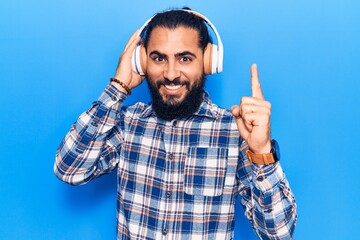 Young arab man listening to music using headphones smiling with an idea or question pointing finger with happy face, number one