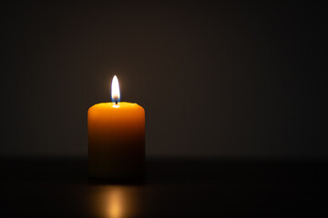 Yellow candle burning on dark background and placed off-center. Minimalist setting with empty space for text on the right