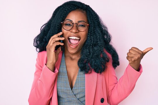 Beautiful african woman having conversation talking on the smartphone pointing thumb up to the side smiling happy with open mouth