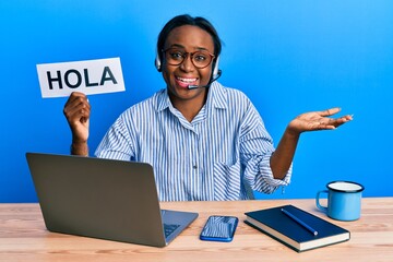 Young african woman wearing operator headset holding hola word celebrating achievement with happy smile and winner expression with raised hand © Krakenimages.com
