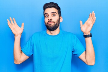 Young handsome man with beard wearing casual t-shirt clueless and confused with open arms, no idea...