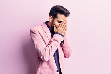 Young handsome man with beard wearing elegant jacket with sad expression covering face with hands...