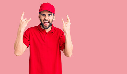 Young handsome man with beard wearing delivery uniform shouting with crazy expression doing rock symbol with hands up. music star. heavy music concept.
