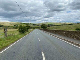 View along, Huddersfield Road, with heavy cloud, fields, and stone walls near, Denshaw, Oldham, UK