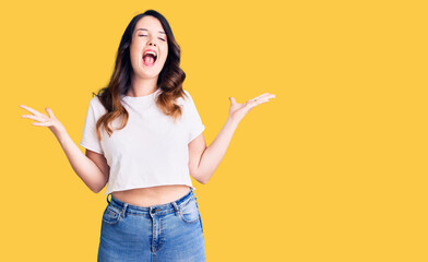 Beautiful young brunette woman wearing casual clothes celebrating mad and crazy for success with arms raised and closed eyes screaming excited. winner concept