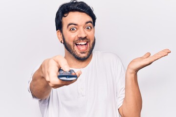 Young hispanic man holding television remote control celebrating achievement with happy smile and winner expression with raised hand