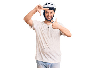 Young hispanic man wearing bike helmet smiling making frame with hands and fingers with happy face. creativity and photography concept.