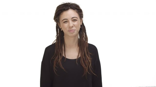 Video of beautiful hippie girl with dreadlocks and ear tunnels, looking happy at camera, starting to smile, standing cheerful over white background