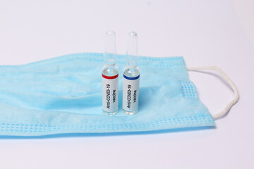 Two medicine ampule with anti covid vaccine on protection mask on white background