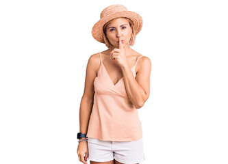 Young blonde woman wearing summer hat asking to be quiet with finger on lips. silence and secret concept.