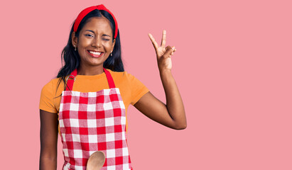 Young indian girl wearing professional baker apron smiling with happy face winking at the camera...