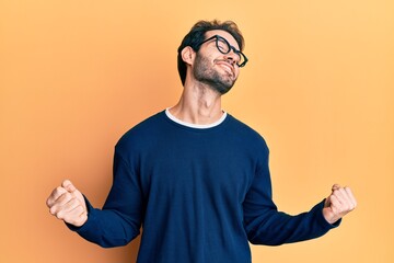 Young hispanic man wearing casual clothes and glasses very happy and excited doing winner gesture...