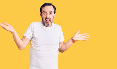 Middle age handsome man wearing casual t-shirt clueless and confused expression with arms and hands...