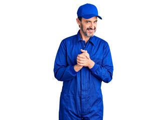Middle age handsome man wearing mechanic uniform with hands together and crossed fingers smiling relaxed and cheerful. success and optimistic