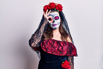 Young woman wearing day of the dead costume over white doing ok gesture with hand smiling, eye looking through fingers with happy face.