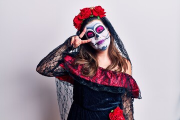 Young woman wearing day of the dead costume over white doing peace symbol with fingers over face, smiling cheerful showing victory