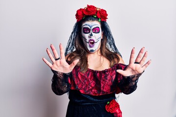 Young woman wearing day of the dead costume over white afraid and terrified with fear expression stop gesture with hands, shouting in shock. panic concept.