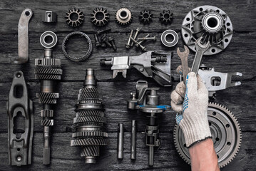 Disassembled parts of a car gearbox and an auto mechanic with a wrench in hand.