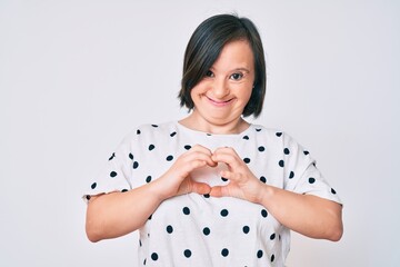 Brunette woman with down syndrome wearing casual clothes smiling in love showing heart symbol and...