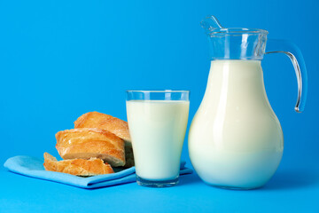 Fresh baguette bread and pitcher with fresh milk on blue background