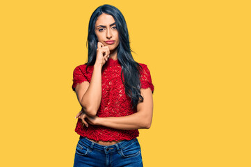 Beautiful hispanic woman wearing elegant shirt serious face thinking about question with hand on chin, thoughtful about confusing idea