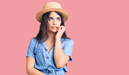 Brunette teenager girl wearing summer hat looking stressed and nervous with hands on mouth biting nails. anxiety problem.