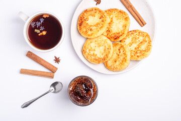 Cottage cheese fritters with fig jam and hot black aromatic tea, Christmas breakfast mood with anise and cinnamon on white background, top view