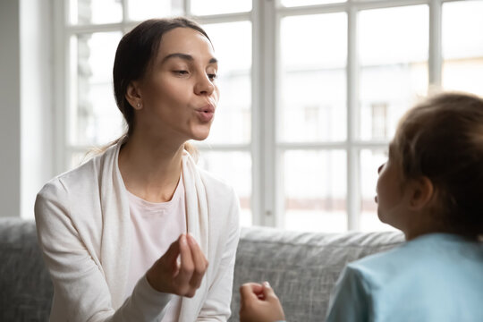 Young Caucasian mom or nanny teach little girl child pronunciation or articulation at home. Caring female teacher or speech therapist have private lesson with small kid, pronounce sounds together.
