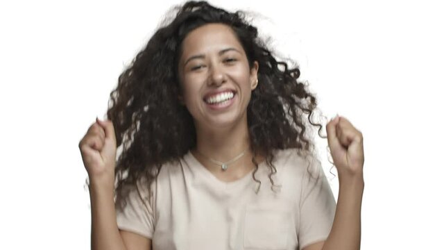 Close-up Of Attractive Curly-haired Woman In Casual T-shirt, Jumping From Happiness, Winning Something And Rejoicing, Raising Hands Up And Smiling, Triumphing Over White Background