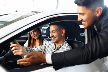 Young couple choosing a car at the dealership with manager helping