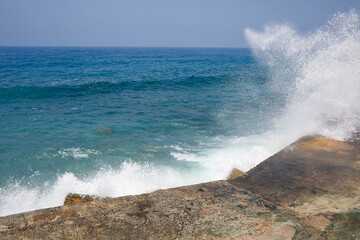 Fototapeta na wymiar Sea water beats against rocky rocks and makes waves with foam