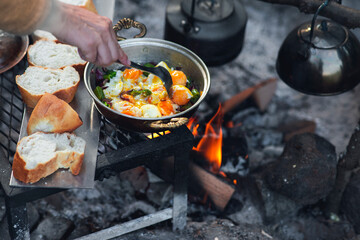 Detail view of camp fire cooking, breads are in a row, a tea pot and onion pan is on the fire with...