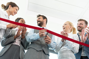 Businessman cutting red ribbon with colleagues at office - obrazy, fototapety, plakaty