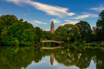 Reflection in lake water of Central Park with a view of trees and bridge in the background