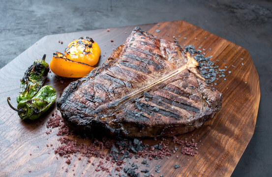 Modern Style traditionelles gegrilltes dry aged Wagyu Porterhouse Steak vom Rind angeboten mit Paprika und Chili als close-up auf einem Design Holz Board