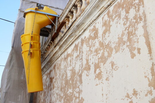 Suspended sections of the yellow garbage chute are attached to the facade of a historic building under construction. Yellow telescope debris chute.