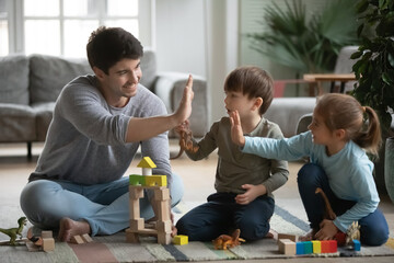 Smiling young dad give high five to excited little kids celebrate good work success playing at home...