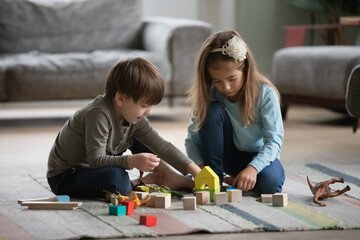 Cute little preschooler boy and girl children sit on warm floor in living room play with building...