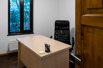 Office room with a desk, a directorial swivel chair, a pen support and some yellow post it papers. - 384645488
