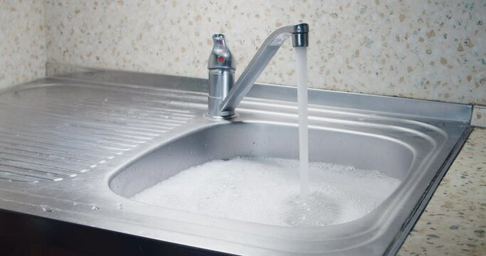 Overflowing kitchen sink with water and foam blockage sin