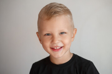 three year old boy in a black t-shirt looks at the camera and smiles. Image with selective focus