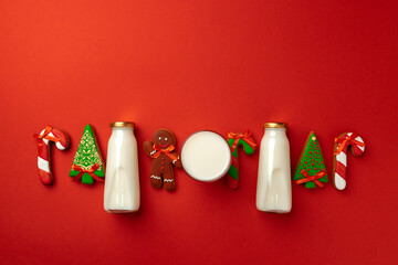 Glass milk bottle and Christmas gingerbread cookies on red background