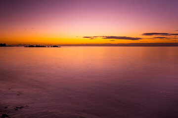 Fototapeta na wymiar Vivid purple glowing sunset over smooth water and rock bird silhouettes
