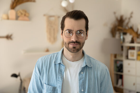 Head Shot Profile Photo Portrait Of Young Pleasant Handsome Man In Eyeglasses. Successful 30s Bearded Freelancer Entrepreneur Businessman Looking At Camera, Posing At Home, Personal Wellbeing Concept.