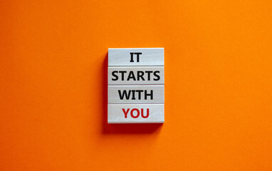 Wooden blocks form the words 'it starts with you' on beautiful orange background. Business concept. Copy space.