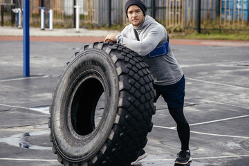 Fototapeta na wymiar Athletic man leans on the tire and rests. Sports field, tire turning, full body exercises