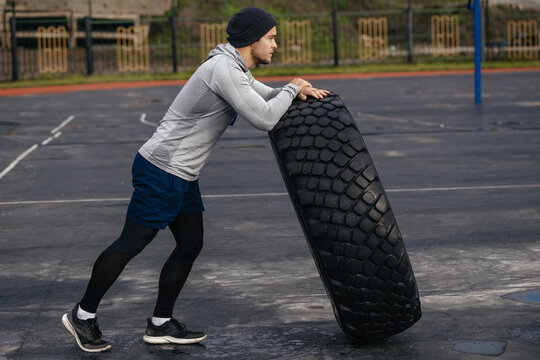 Strong, Big, Beefy Man Lifts A Tire. The Concept Of A Strong Healthy Lifestyle. The View From The Side