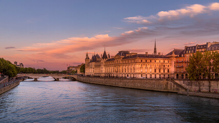 Paris, France - August 28, 2020: View of Seine river with Conciergerie palace, bridge over the Seine river and Parisians walking on the embankment at sunset